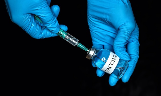 Photo main en gants médicaux bleus tenant une bouteille de verre avec l'étiquette du vaccin sur fond noir