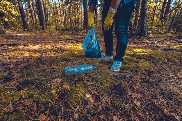 Photo une main avec des gants ramasse une bouteille en plastique du sol et la place dans un sac à ordures un volontaire