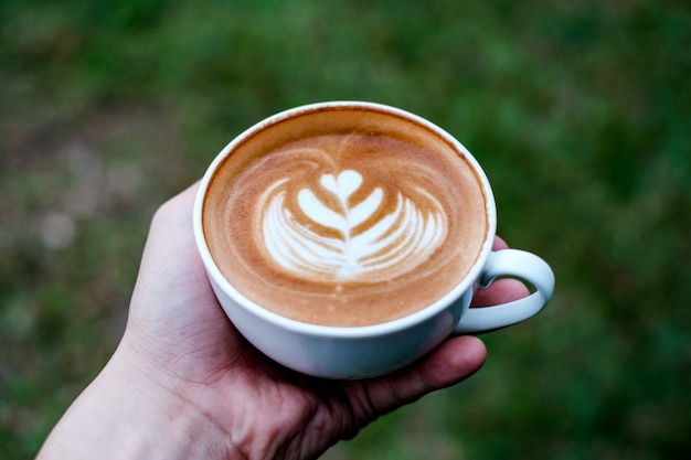 Main gauche tenant tasse à café Latte avec forme de coeur dans la forêt