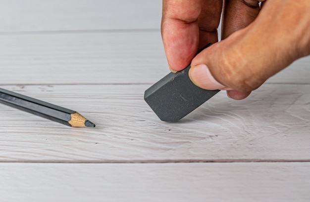 Main avec une gomme noire et un crayon sur une table blanche