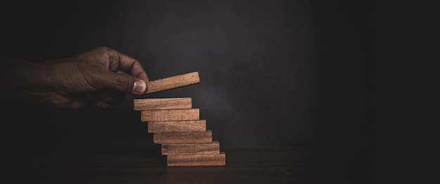 La main en gros plan place la tour de bloc de bois empilée dans l'étape d'escalier