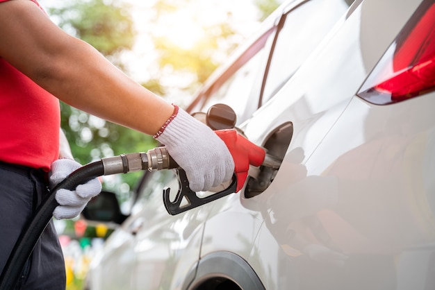 La main en gros plan d'un travailleur de ravitaillement en gaz portant des gants ravitaille les clients, l'équipement de pompage de gaz à la station-service.