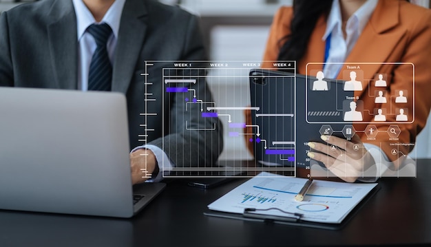 Main d'homme d'affaires Chef de projet travaillant et mettant à jour les tâches et le diagramme virtuel de planification du diagramme de Gantt avec une tablette de téléphone intelligent et un ordinateur portable au bureau