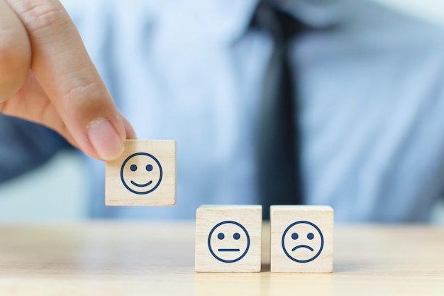 Main d'un homme d'affaires choisit un visage souriant sur un cube en bloc de bois, Le meilleur excellent service clients pour évaluer les services aux entreprises, Concept d'enquête de satisfaction