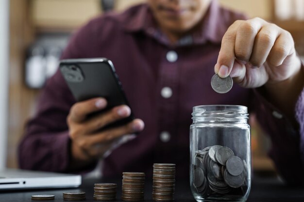 Main d'homme d'affaires mettant des pièces dans du verre pour économiser de l'argent concept finance et comptabilité à la maison