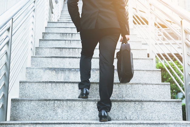 Main d'homme d'affaires moderne tenant une mallette à côté de travail de près les jambes en montant les escaliers dans la ville moderne. aux heures de pointe pour travailler au bureau pressé.