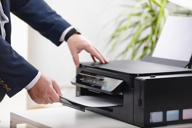 Main d'homme d'affaires prenant du papier du scanner de l'imprimante ou de la photocopieuse laser au bureau