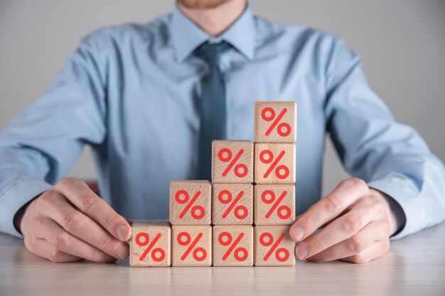 La main d'homme d'affaires prend un bloc de cube en bois représentant, montré l'icône de symbole de pourcentage. Concept de taux d'intérêt financiers et de taux hypothécaires.
