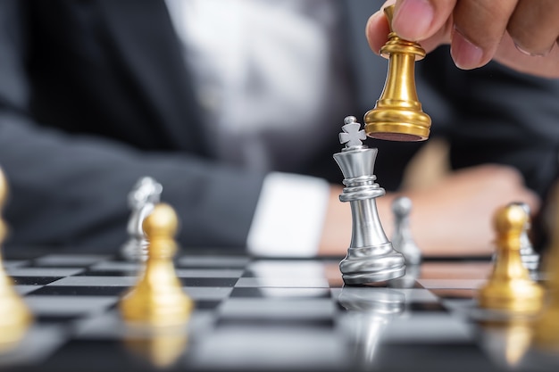 Main d'homme d'affaires se déplaçant en or Chess King figure et Checkmate enermy ou adversaire lors de la compétition d'échecs.