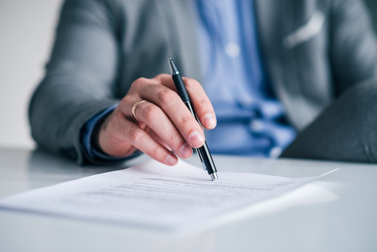Photo main d&#39;homme d&#39;affaires tenant le stylo sur le contrat, document sur la table blanche, gros plan.