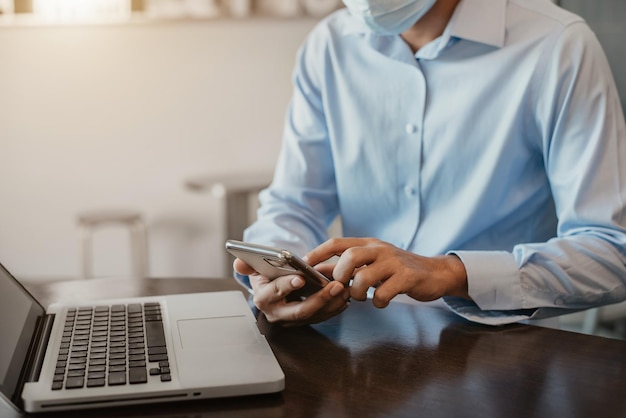 Main d'homme d'affaires travaillant avec un téléphone intelligent et un ordinateur portable dans un bureau moderne