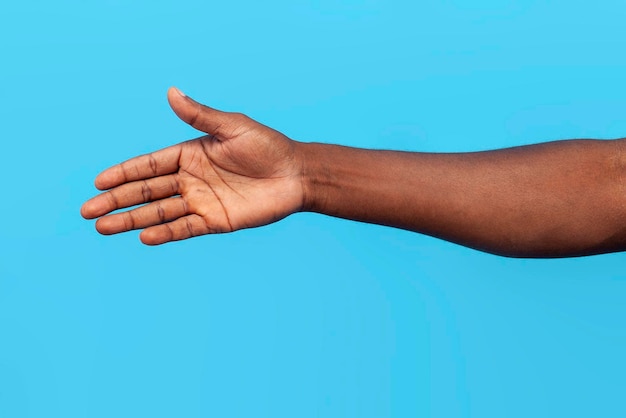 main d'un homme afro-américain montrant une paume vide et un geste de poignée de main sur fond bleu en gros plan