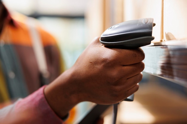 Photo main d'homme afro-américain tenant un scanner de codes-barres dans un entrepôt industriel. bras de travailleur d'entrepôt de fret scannant le code de la boîte en carton du fret pour la gestion des stocks en gros plan