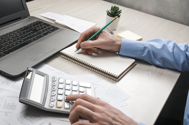 Main de l'homme à l'aide de la calculatrice et de l'écriture prendre note avec calculer le coût et les taxes au bureau à domicile. Homme d'affaires faisant de la paperasse sur le lieu de travail