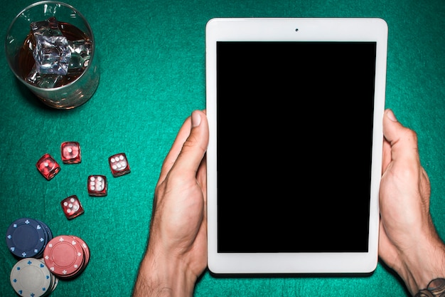 La main de l&#39;homme à l&#39;aide d&#39;une tablette numérique sur la table de poker avec un verre à whisky