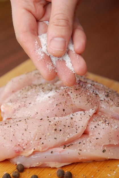 Main de l'homme ajoutant du sel aux poitrines de poulet crues. Régimes amaigrissants, aliments sains à faible teneur en calories, concept de préparation de repas