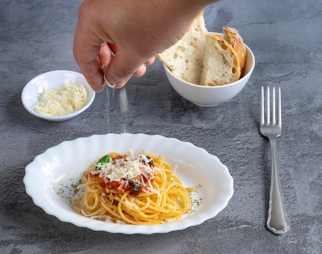 La main de l'homme ajoute du parmesan sur une assiette de pâtes italiennes à la sauce amatriciana. Prêt à manger,