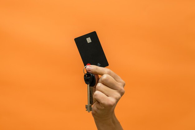 La main de l'homme avec clés et carte de crédit isolé sur fond orange
