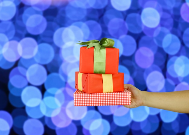 Main de l'homme avec un coffret cadeau de Noël rouge sur fond bleu bokeh.