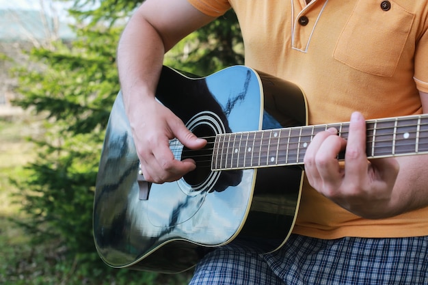 Main de l'homme à cordes de guitare en plein air