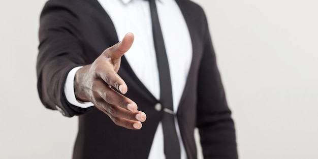 Main de l'homme en costume noir et cravate donnant la main à la salutation ou à la poignée de main à la caméra. se concentrer sur la main. tourné en studio intérieur, isolé sur fond gris clair.