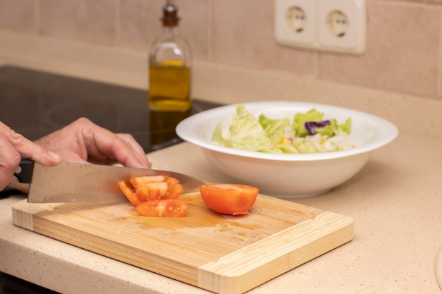 La main d'un homme coupant une tomate avec un couteau sur une planche de bois Mise au point sélective