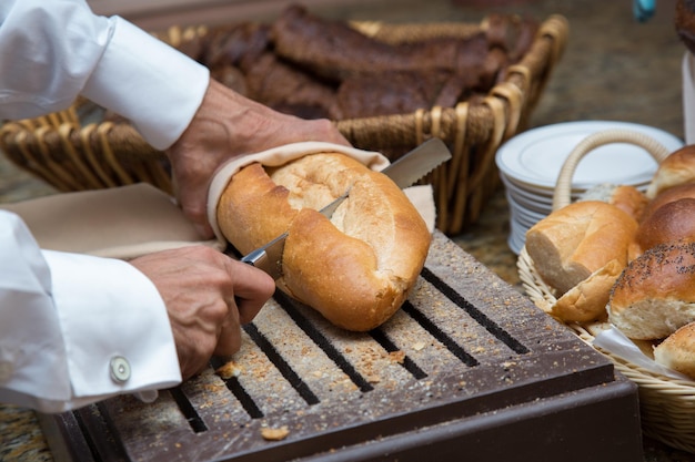 La main de l'homme coupe du pain sur une planche de bois avec un couteau