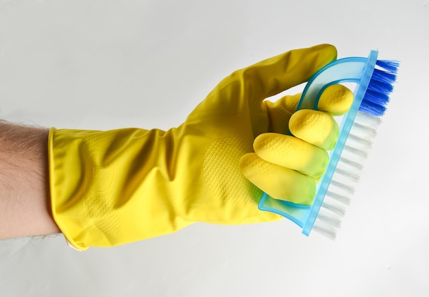 La main d'un homme dans un gant en latex jaune tient une brosse en plastique. Concept de nettoyage