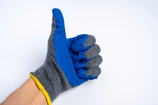 Une main d'homme dans des gants de travail caoutchoutés bleus montre un pouce levé sur un fond bleu