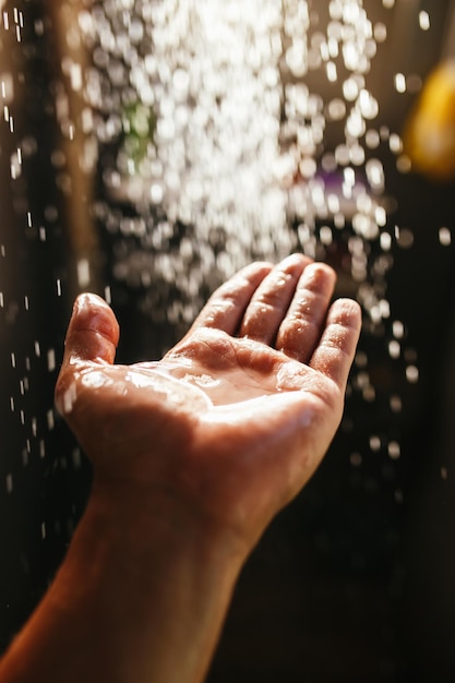 La main d'un homme dans un jet d'eau au soleil sur un fond sombre.