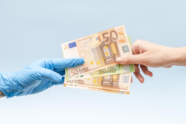 Main de l'homme donnant de l'argent euro à une main dans un gant chirurgical bleu infirmière ou médecin Corruption en médecine