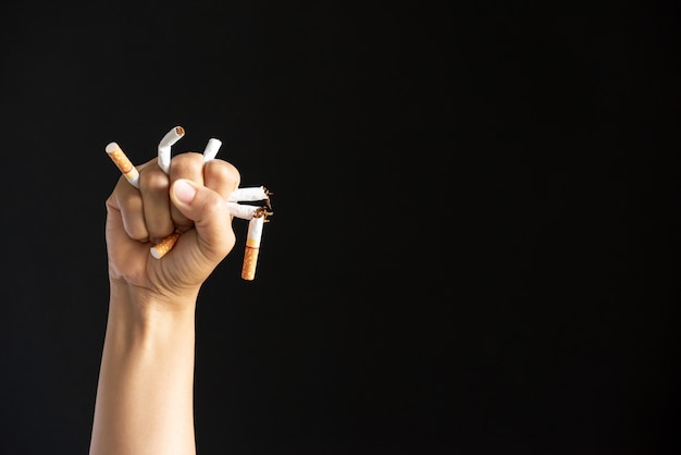 Main d&#39;homme écrasant et détruisant des cigarettes sur fond noir.