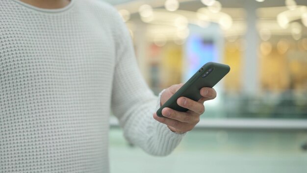 Main de l'homme faisant défiler un téléphone sur fond jaune flou