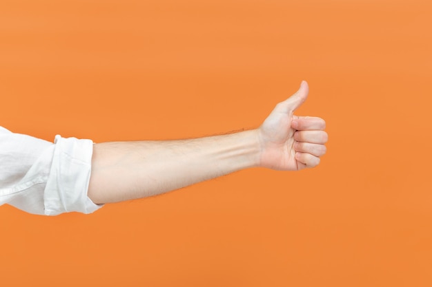 La main d'un homme faisant un signe de pouce vers le haut sur un fond orange. Notion de langage corporel. Signe de la main. Comme un geste.