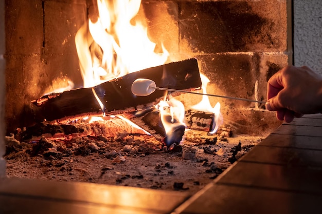 Photo la main de l'homme fait frire une délicieuse guimauve sucrée sur un feu dans une cheminée à foyer ouvert par une journée froide