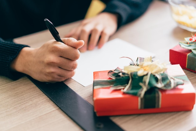 La main de l'homme en gros plan écrit sur une carte postale de Noël vierge avec un stylo Couple assis et écrivant une carte de Noël ensemble pour l'envoyer avec des cadeaux surprises à la maison pendant les vacances de Noël