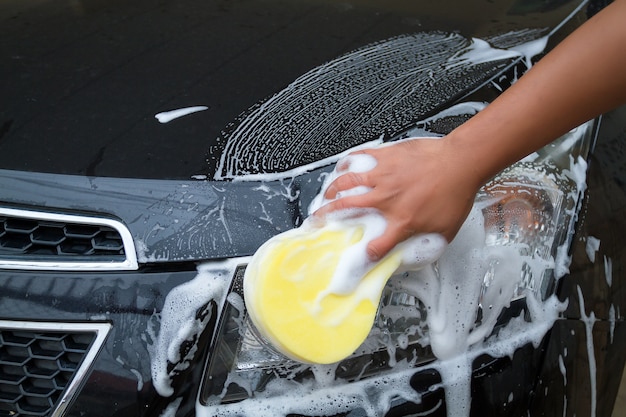 main de l&#39;homme laver la voiture en utilisant l&#39;éponge jaune avec de la mousse