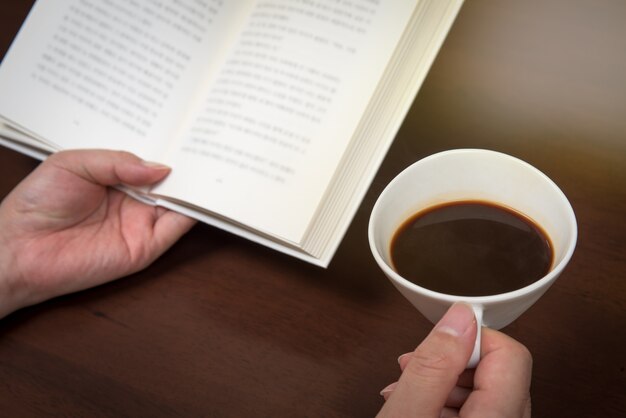 La main de l'homme lisant avec une tasse de café à la main.