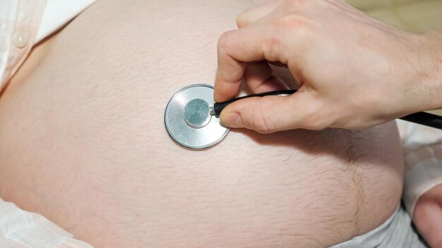 La main d'un homme méconnaissable conduit un stéthoscope sur le gros ventre d'une femme enceinte