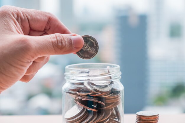 Main d&#39;homme mettant la pièce dans le verre de la bouteille pour économiser de l&#39;argent