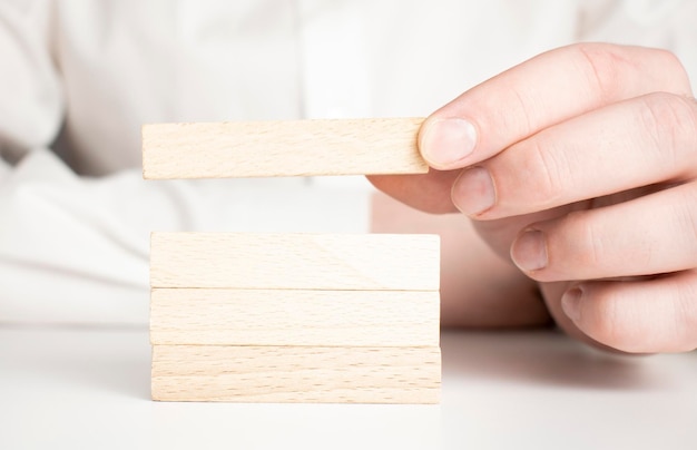 La main de l'homme a mis des blocs de bois sous la forme d'un escalier isolé sur fond blanc avec espace de copie Concept de fondation de succès de construction