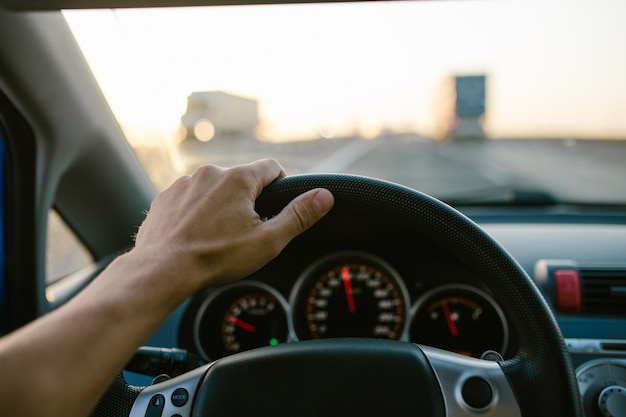 Photo la main de l'homme de mise au point sélective sur le volant, conduisant une voiture au coucher du soleil. fond de voyage.