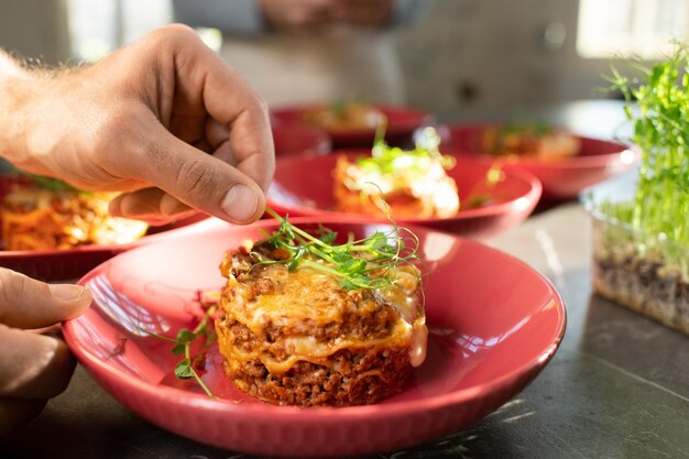 Main d'homme mûr mettant une branche de semis de soja décoratif vert frais sur un plat de viande appétissant fait maison sur une assiette en porcelaine rouge