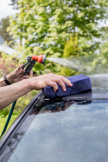 Main de l'homme nettoyant la voiture noire par une éponge et un tuyau.