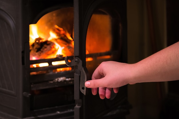 Main de l'homme ouvrant une porte de la cheminée avec des bûches en bois brûlant à l'intérieur