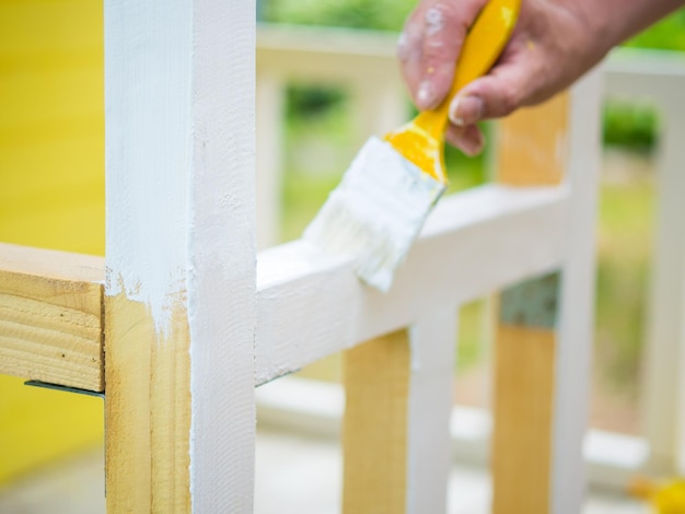 La main d'un homme avec un pinceau peint une poutre en bois avec de la peinture blanche