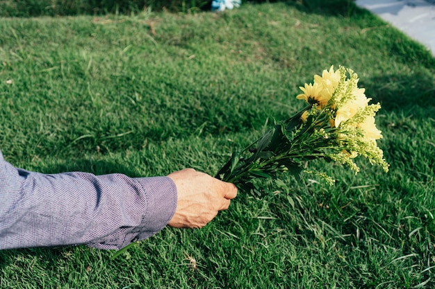 Main d'un homme plaçant des fleurs sur la tombe dans un cimetière