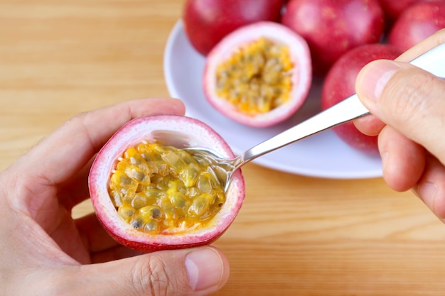 La main de l'homme prélevant des fruits de la passion frais et mûrs de sa coquille avec une cuillère