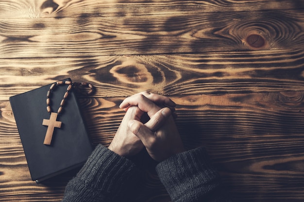 La main de l'homme de prière croix sur Sainte Bible sur table en bois