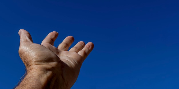 Une main d'homme s'approchant du ciel bleu. symbole de la foi
